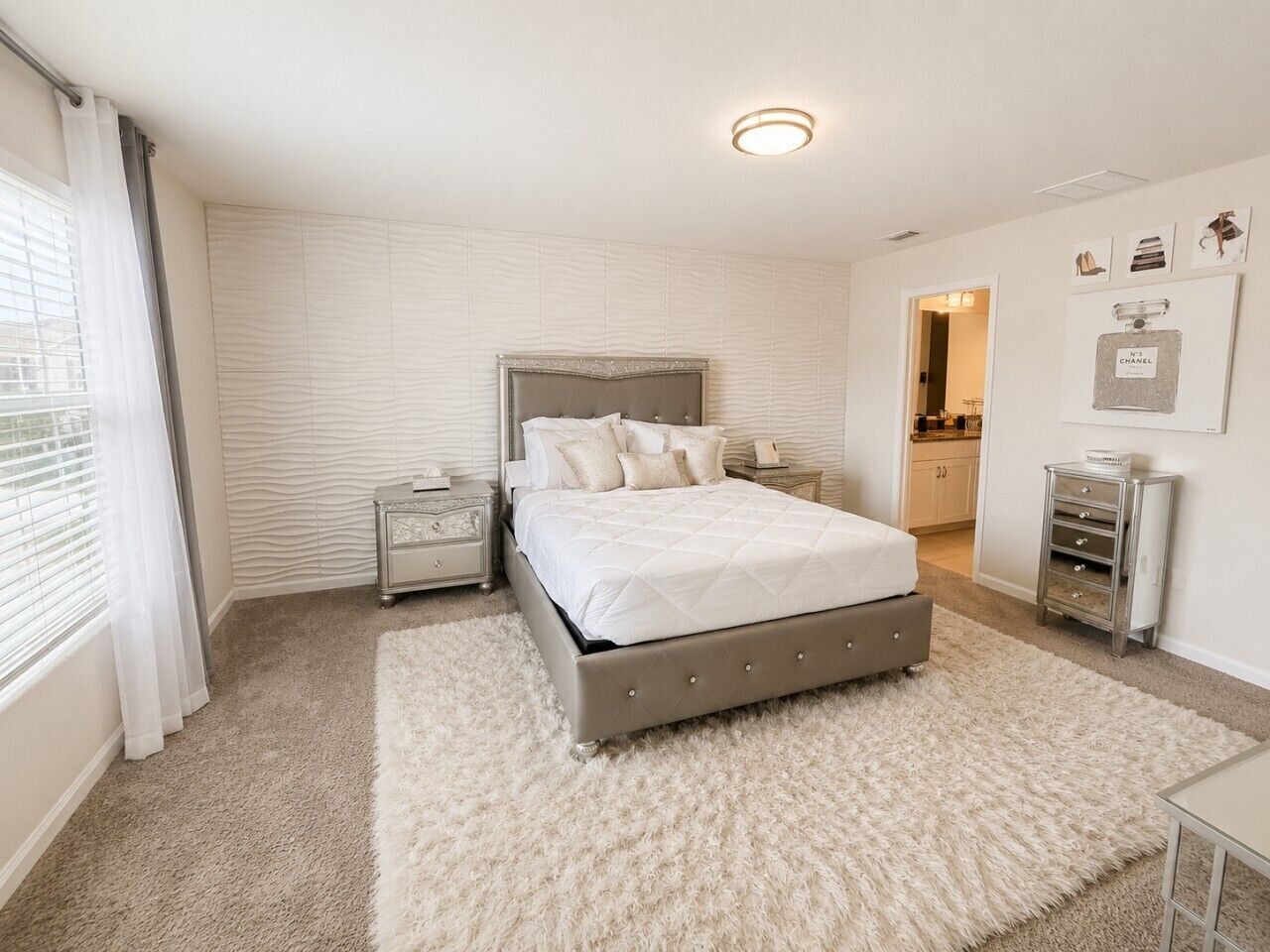 A bedroom with a large bed, a nightstand, a dresser, and a window with curtains.