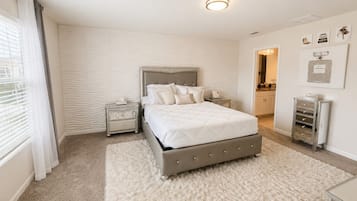 A bedroom with a large bed, a nightstand, a dresser, and a window with curtains.