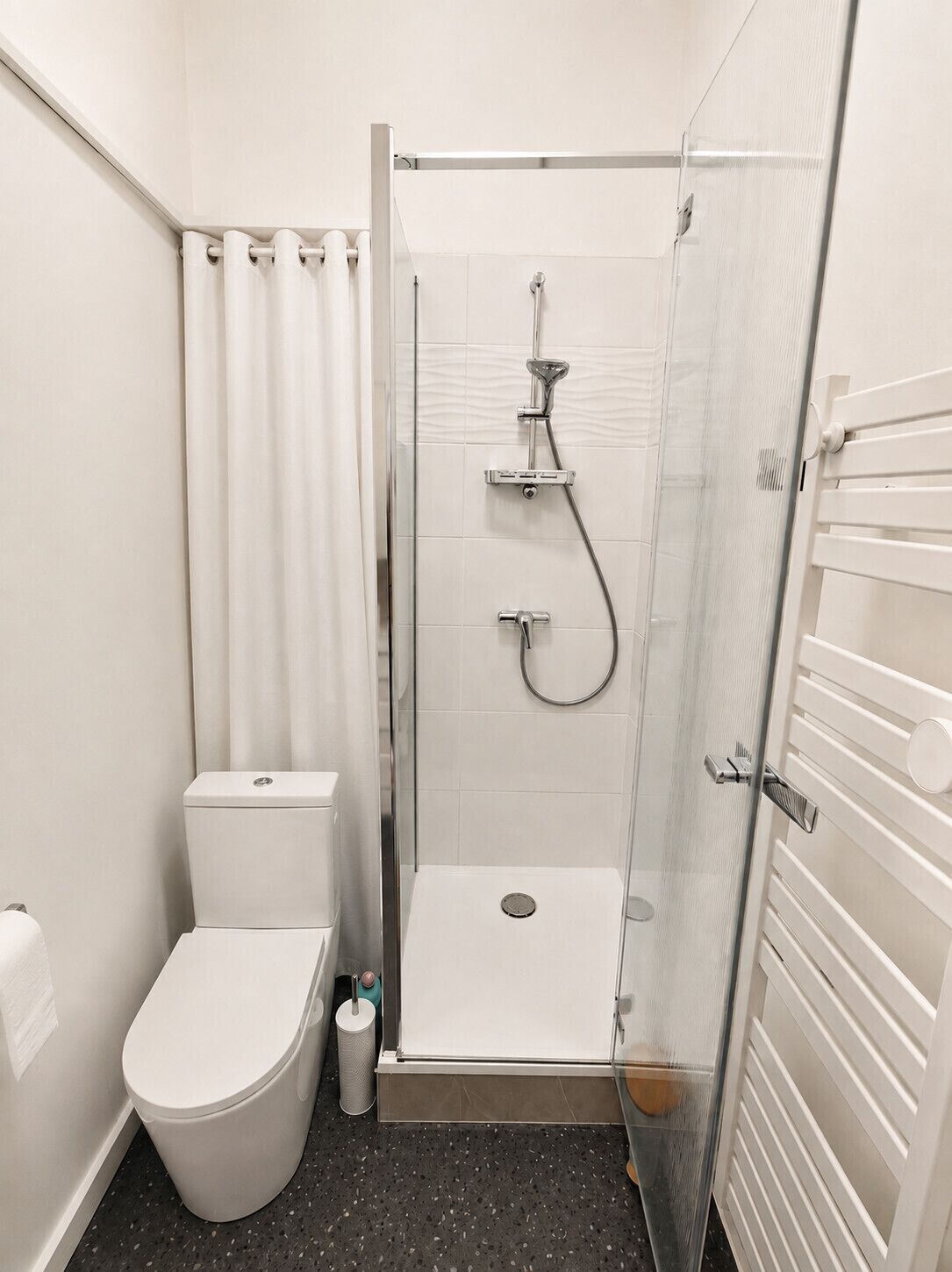 A modern bathroom with a glass-enclosed shower, a toilet, and a towel rack.