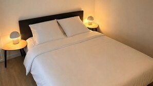 Un lit bien fait, avec du linge de lit blanc, deux lampes de chevet et une table de chevet ronde en bois.