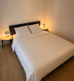 A neatly made bed with white linens, two bedside lamps, and a round wooden nightstand. - Les Embruns - Quartier Arago (Les Sables-d´Olonne)