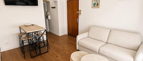 Ein Wohnzimmer mit einer Couch, einem Couchtisch, einem an der Wand befestigten Fernseher und einer Tür zu einem anderen Raum.