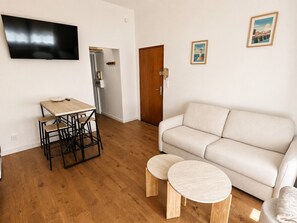 Ein Wohnzimmer mit einer Couch, einem Couchtisch, einem an der Wand befestigten Fernseher und einer Tür zu einem anderen Raum.