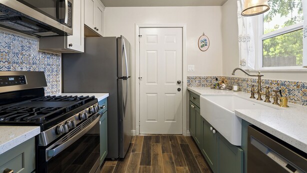Una cocina con estufa, refrigerador y ventana con vistas a árboles.