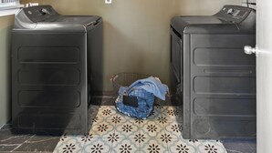 Un lavadero con dos lavadoras, un ventilador de techo y piso de baldosas.