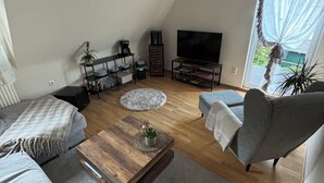 Moderni olohuone, jossa on sohva, sohvapöytä, televisio ja kirjahylly.