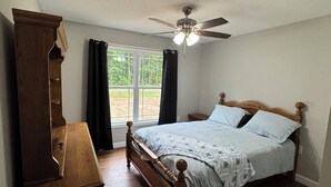 A bedroom with a wooden bed, a nightstand, a dresser, a ceiling fan, and a window with curtains. -  Peaceful Country Getaway 3BR • 2BA • Fire Pit • Near Outdoor Adventures (Clarkrange)