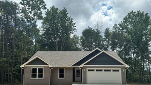 A single-story house with a garage, surrounded by a forest. -  Peaceful Country Getaway 3BR • 2BA • Fire Pit • Near Outdoor Adventures (Clarkrange)