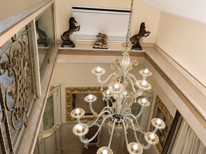 A grand chandelier with multiple light fixtures, ornate wall mirrors, and decorative horse statues on a high ceiling. - Villa on the Lido of Venice, for those seeking luxury, convenience close Venice. (Venezia)