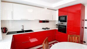 A modern kitchen with white and red cabinetry, a stainless steel sink, and a built-in oven. - Villa on the Lido of Venice, for those seeking luxury, convenience close Venice. (Venezia)