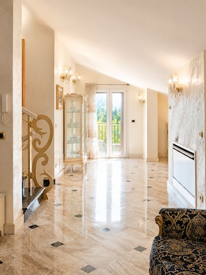 A spacious hallway with a marble floor, a staircase with ornate gold railings, and a large window offering a view of greenery. - Villa on the Lido of Venice, for those seeking luxury, convenience close Venice. (Venezia)