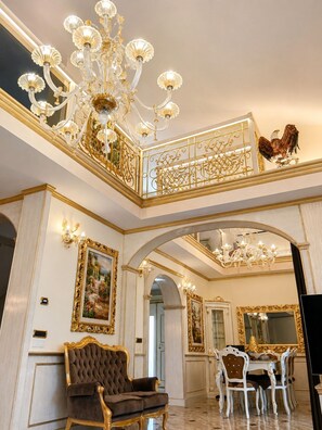 A luxurious interior with a grand chandelier, ornate gold detailing, and a dining area with white chairs. - Villa on the Lido of Venice, for those seeking luxury, convenience close Venice. (Venezia)