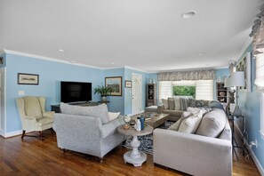 A living room with a television, two armchairs, a sofa, a coffee table, and a window with curtains. - Horsing around across the street from Bruce's Field. (Aiken)