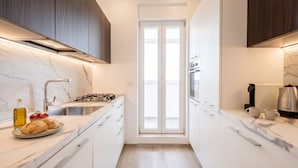Eine schmale Küche mit weißen Schränken, einer Marmorarbeitsplatte und einem eingebauten Backofen.