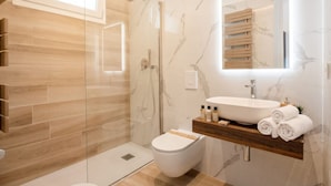 Ein modernes Badezimmer mit einer Glasdusche, einer weißen Toilette, einem Holzwaschtisch und einer Marmor-Spritzschutzwand.
