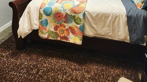 Quarto com cama, ventilador de teto, luminária na parede e cortina estampada.