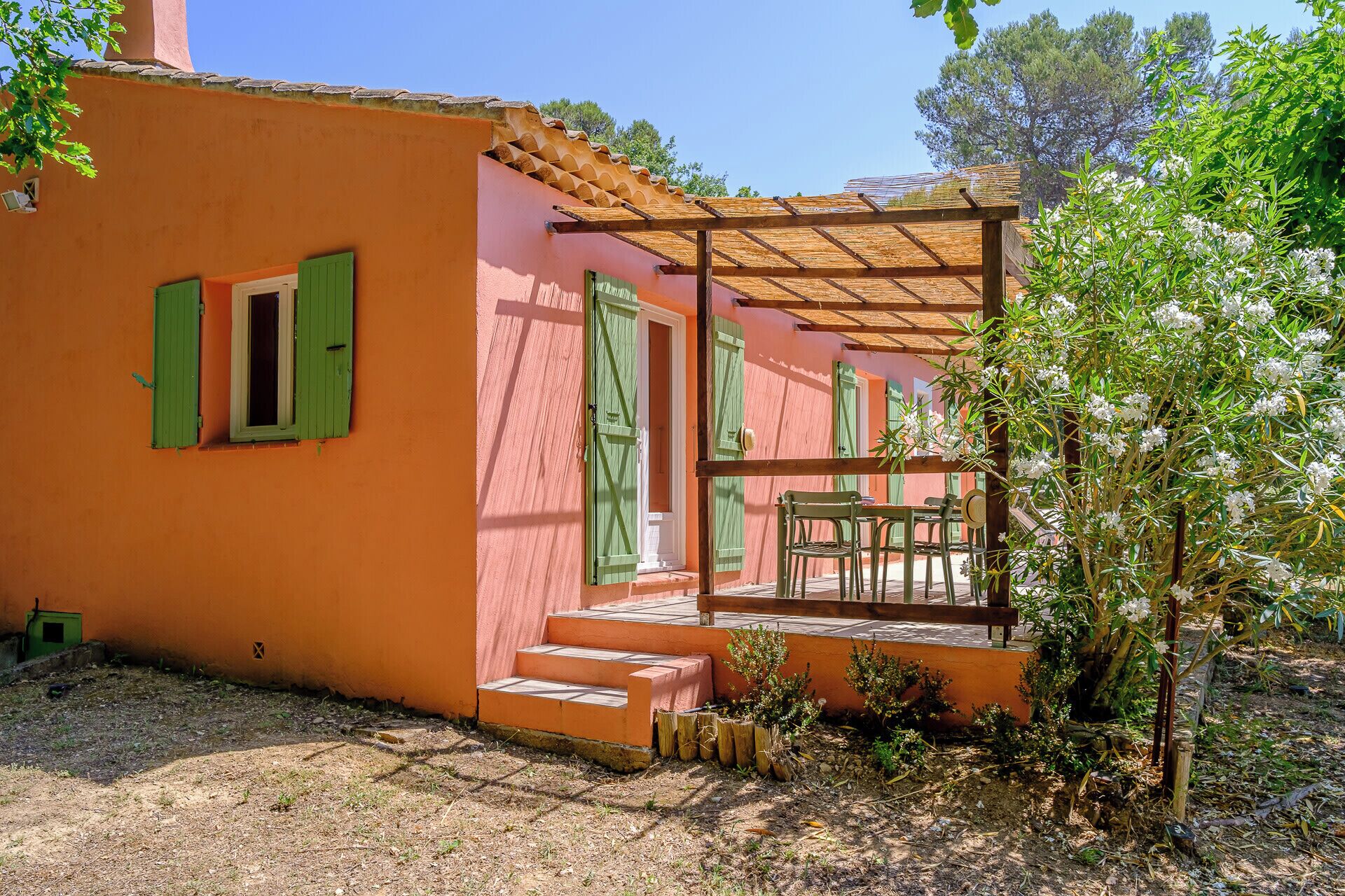 A building with a pink exterior, green shutters, and a wooden pergola.