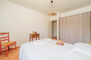 A bedroom with a bed, a chair, a small table, and a door leading to another room. - Maison Vigneron | Domaine Tour Campanets (Le Puy-Sainte-Réparade)