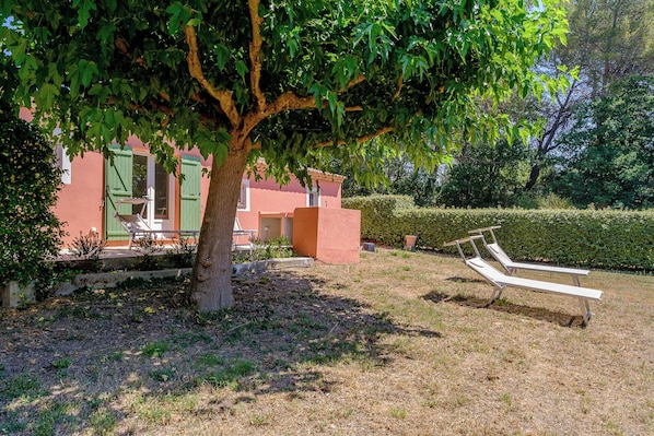 A garden with a tree, a bench, and a building with a green door. - Maison Vigneron | Domaine Tour Campanets (Le Puy-Sainte-Réparade)