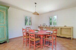 A dining area with a round table and six chairs, a cabinet, and a window with a view of greenery. - Maison Vigneron | Domaine Tour Campanets (Le Puy-Sainte-Réparade)