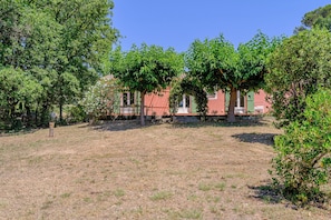A building with a red facade, surrounded by trees and a grassy area. - Maison Vigneron | Domaine Tour Campanets (Le Puy-Sainte-Réparade)