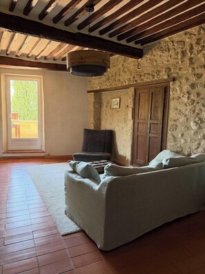 Ein Zimmer mit Steinwand, Holzboden, einer Couch, einer Tür und einem Fenster.