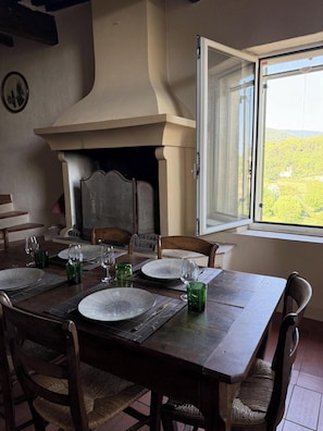 A dining area with a fireplace, a table set for four, and a view of the countryside through a window. - Gorgeous 3-bedroom house with AC in Cabrières-d'Aigues (Cabrières-d'Aigues)