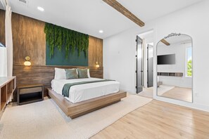 Een moderne slaapkamer met een houten hoofdbord, een bed met witte beddengoed, een hangende groene plant en een grote spiegel.