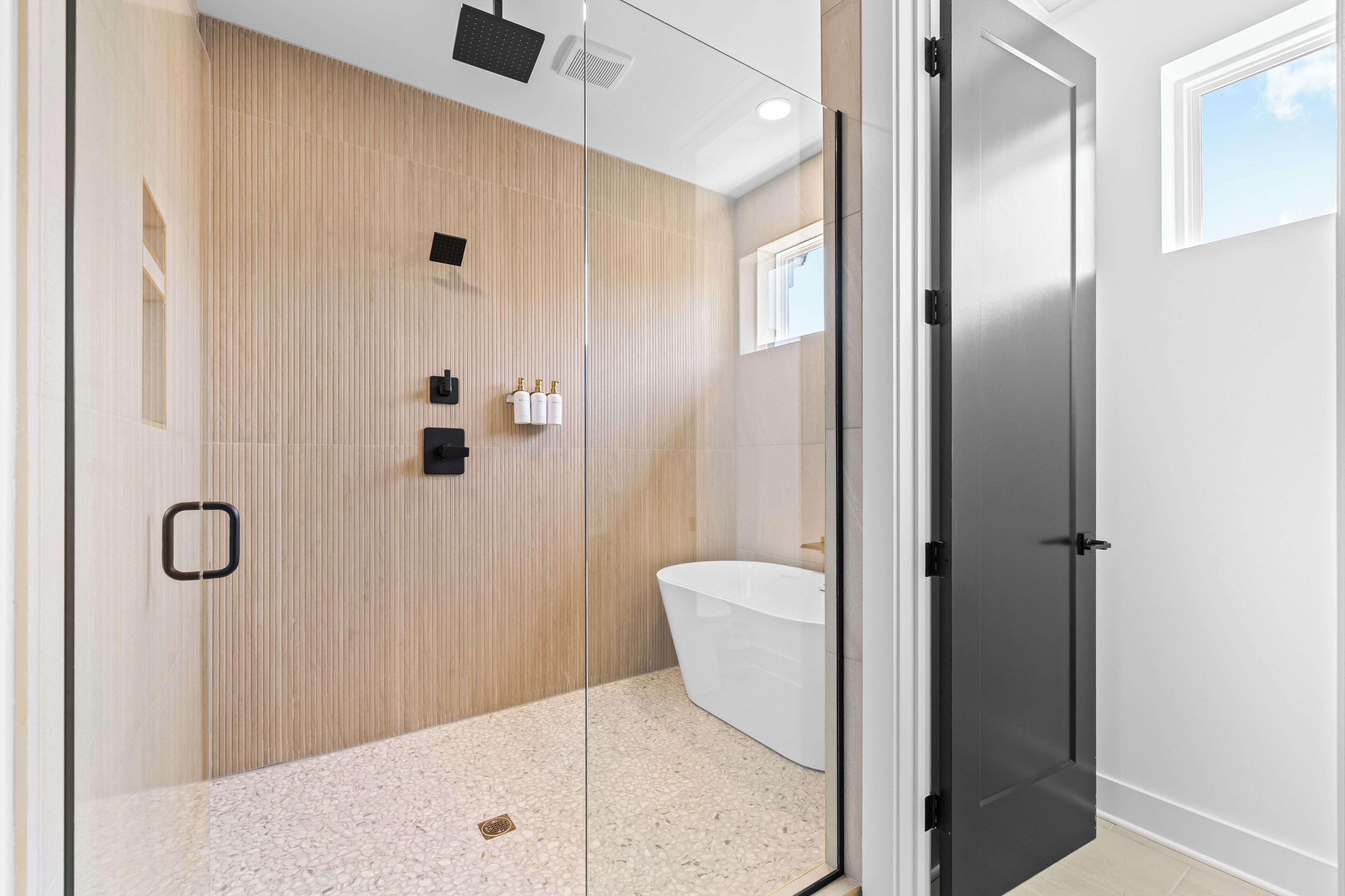 A modern bathroom with a freestanding bathtub, a shower area, and a glass door leading to the room.