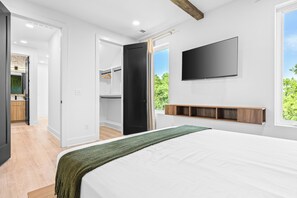 Ein Schlafzimmer mit einem Bett, einem an der Wand montierten Fernseher und einem Fenster mit Blick auf Grünflächen.