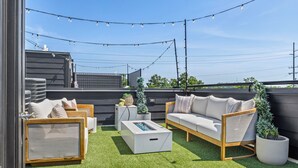 An outdoor seating area with a sofa, chairs, and a coffee table, surrounded by artificial grass and string lights. - NEW Home with Luxury Wet Room & Rooftop Hot Tub 8 to Broadway (Nashville)