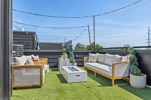 Ein Außenbereich mit Sitzgelegenheiten, darunter eine Couch, Stühle und ein Couchtisch, umgeben von Kunstgras und Lichterketten.
