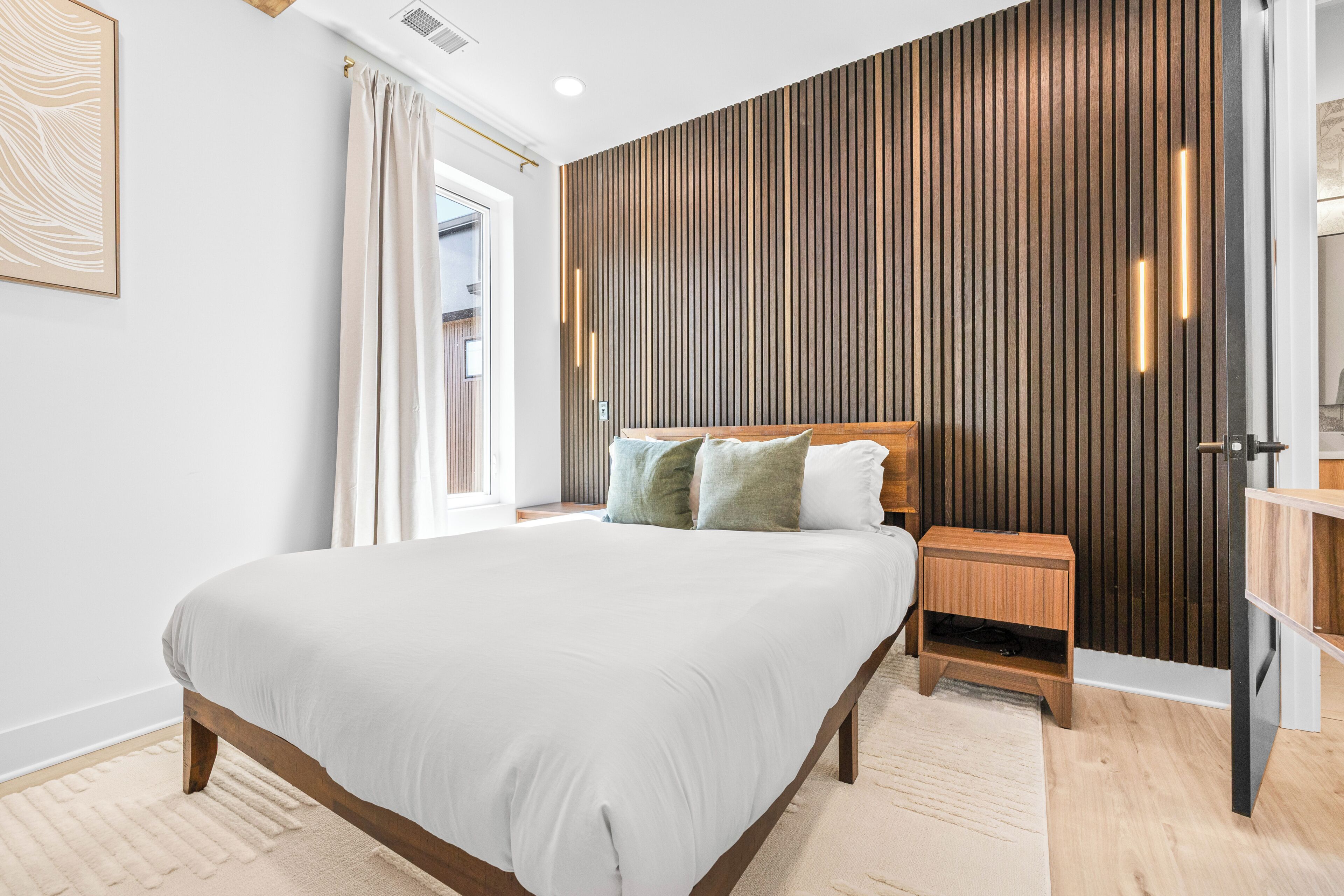 Een moderne slaapkamer met een groot bed, een houten hoofdbord, een nachtkastje en een wand van houten panelen.