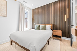 A modern bedroom with a large bed, a wooden headboard, a nightstand, and a built-in wooden panel wall. - NEW Home with Luxury Wet Room & Rooftop Hot Tub 8 to Broadway (Nashville)