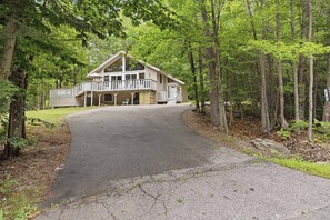 A two-story lodge with a covered porch and a driveway leading to the entrance. - Family Cabin Near Story Land & Attitash (Bartlett)