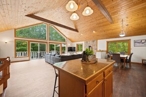 A spacious living area with a large wooden ceiling, a central island with a granite countertop, and a seating area with a gray sofa. - Family Cabin Near Story Land & Attitash (Bartlett)