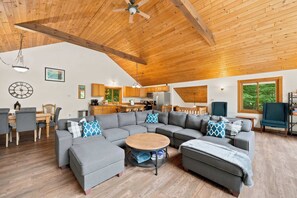 Een ruime woonkamer met een grote modulaire bank, een ronde salontafel en een eethoek met een houten tafel en stoelen.