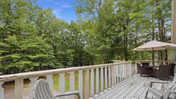 Una terraza de madera con mobiliario exterior y barandilla con vista a un bosque.
