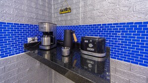 Una cocina con salpicadero de azulejos azules, una cafetera, un tostador y un hervidor sobre la encimera.