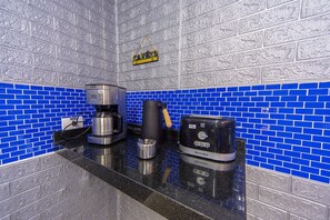 Eine Küche mit dunkelblauer Fliesenspiegel, einer Kaffeemaschine, einem Toaster und einem Wasserkocher auf der Arbeitsfläche.