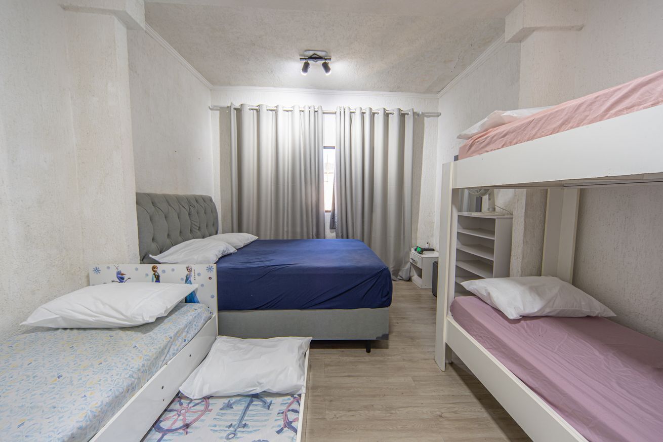 Une chambre avec un lit simple, un lit superposé, une table de chevet et une fenêtre avec des rideaux.