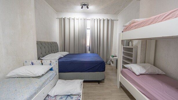 Un dormitorio con una cama individual, una litera, una mesita de noche y una ventana con cortinas.