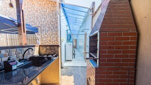 Una cocina exterior estrecha con horno de ladrillo, pileta y parrilla.