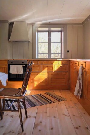 A kitchen with wooden cabinets, a window, a chair, and a rug. - Authentic 1800s cottage in Småland (Svenstorp)