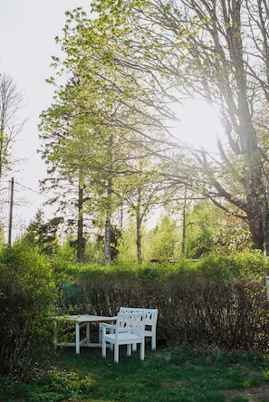 A white bench and table set in a lush green outdoor area with trees and bushes. - Authentic 1800s cottage in Småland (Svenstorp)
