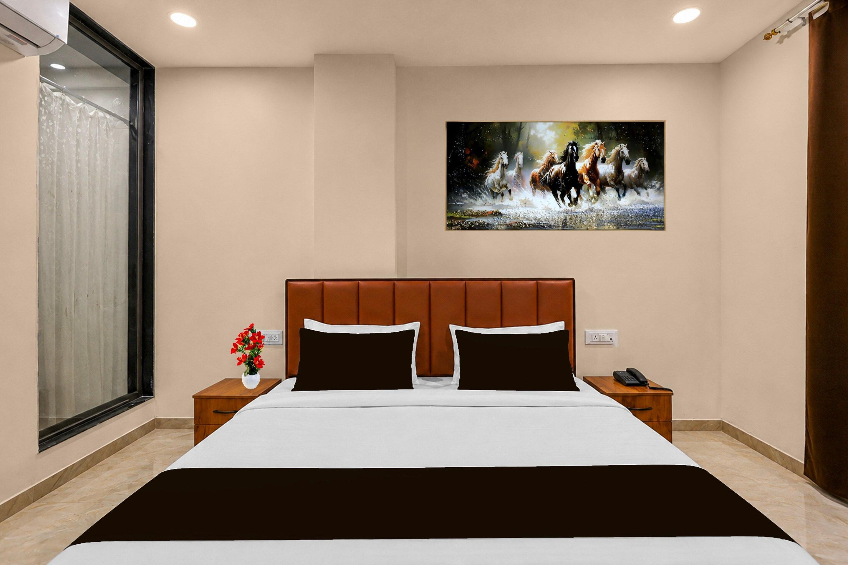 A hotel room with a large bed, two nightstands, a painting of horses, and a window with curtains.