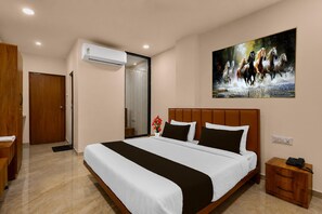 A hotel room with a large bed, a painting of horses, an air conditioning unit, and a wooden nightstand. - Classic Golden Retreat Hotel (Anand)
