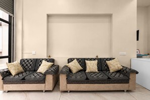 Two sofas with patterned upholstery and matching cushions, positioned in a room with a plain wall and a window to the left. - Classic Golden Retreat Hotel (Anand)