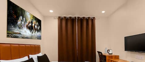 A hotel room with a bed, a desk, a television, and a painting of horses on the wall.