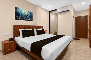 A hotel room with a bed, bedside table, and an air conditioning unit. - Classic Golden Retreat Hotel (Anand)